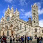 a large building with many people in front of it with Siena Cathedral in the background